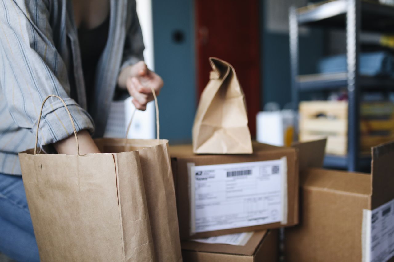 about-us-01 Woman sorting parcels and paper bags in a home setting, showcasing online shopping and delivery.