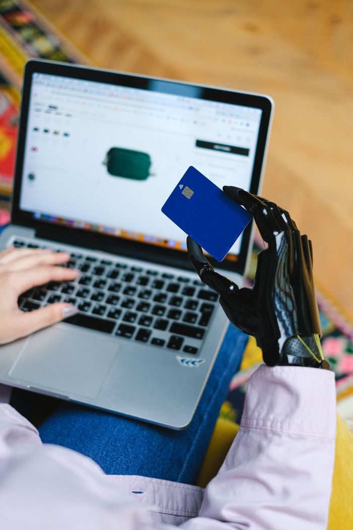 services-03 Person with prosthetic hand using laptop for online shopping, holding a credit card.