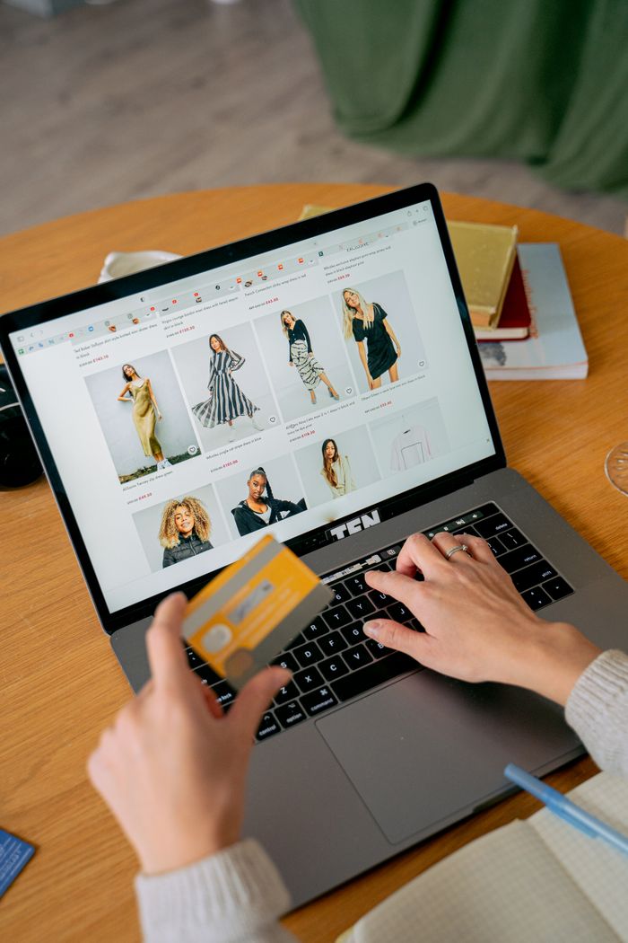 A woman makes an online purchase using a credit card on her laptop, browsing an online fashion store.